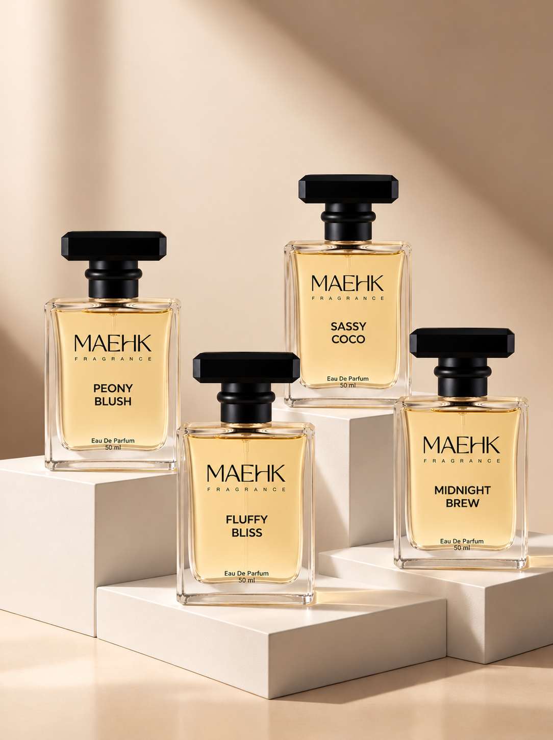 Four MAEIK Fragrances Eau De Parfum bottles arranged on white geometric pedestals against a warm beige background. The bottles contain pale golden-yellow liquid and have black caps.